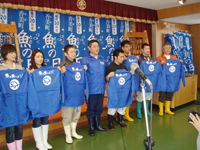 室内で青いジャンパーを掲げて魚の日のPRをする人たちの写真