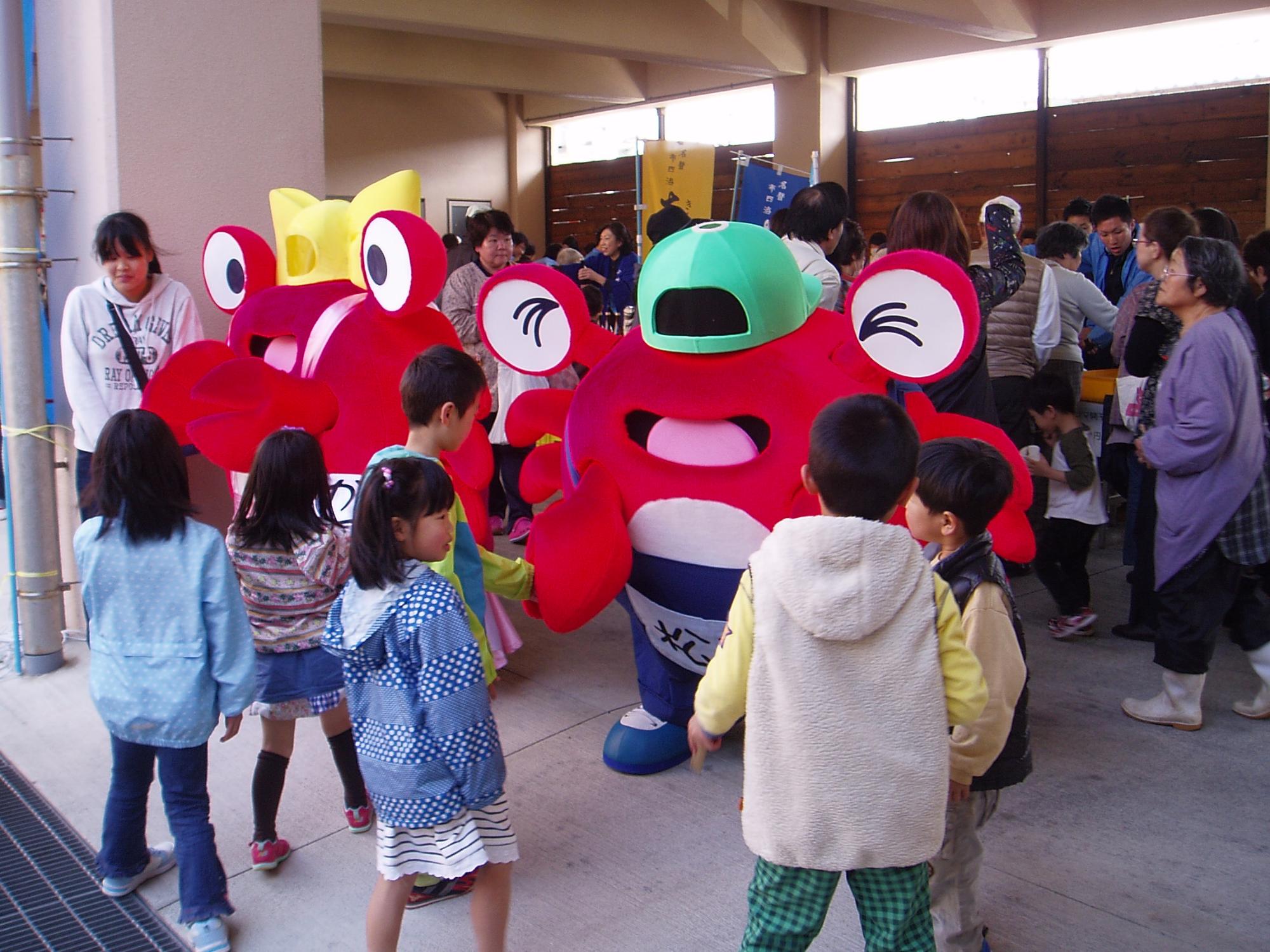 イベント会場でカニの着ぐるみキャラクターと子どもたちが触れ合っている写真