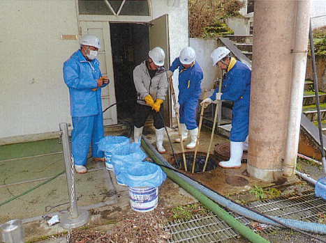 作業員が下水道管の付近で詰まりの解消作業を行っている様子の写真