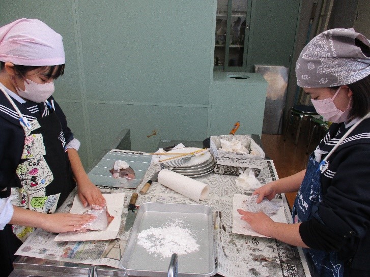 生徒たちが魚に衣をつけている様子の写真