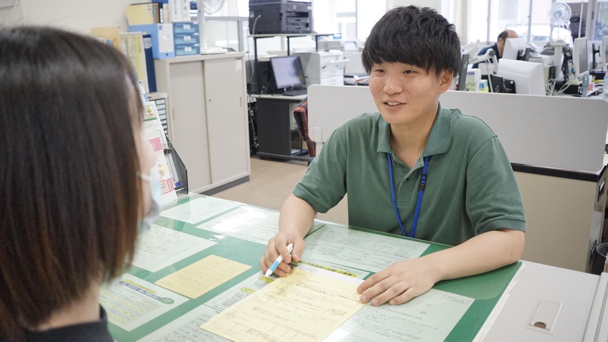 笑顔で机越しに話している緑色の服を着た町役場職員の写真
