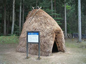 案内看板が置かれたかやでできた竪穴式住居の写真
