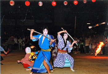 顔を白く化粧した青と紫の着物を着た2人が刀を構えている写真