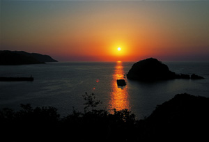 水面近くにあるオレンジ色の太陽と海に移るオレンジ色の太陽の光の写真