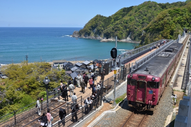 海沿いの駅に停まる赤紫色の電車の写真