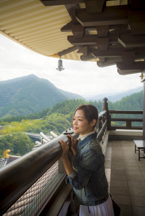 お寺の建物の高いところから景色を眺める女性の写真