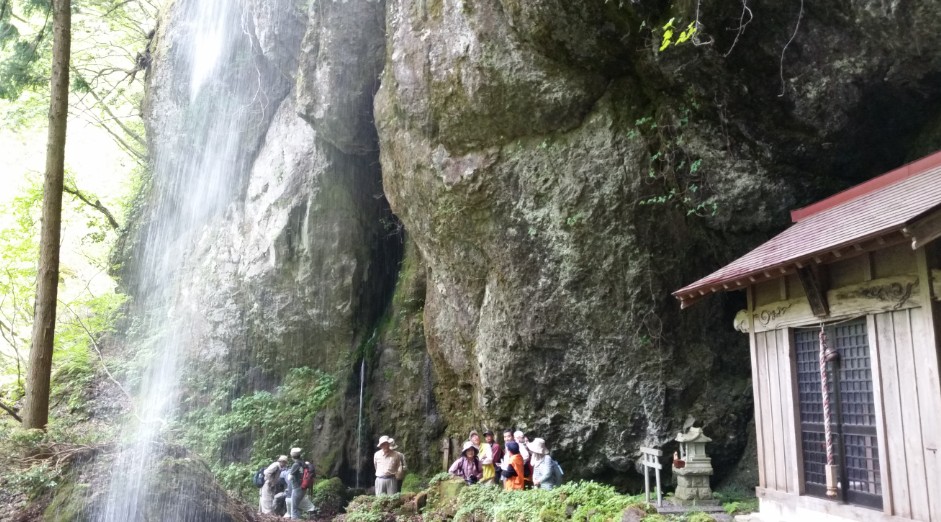神社の脇にある大きな岩と滝の間に集まる人たちの写真