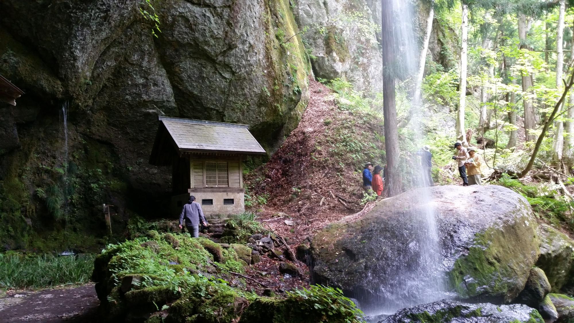 滝と祠の間を歩く人たちの写真