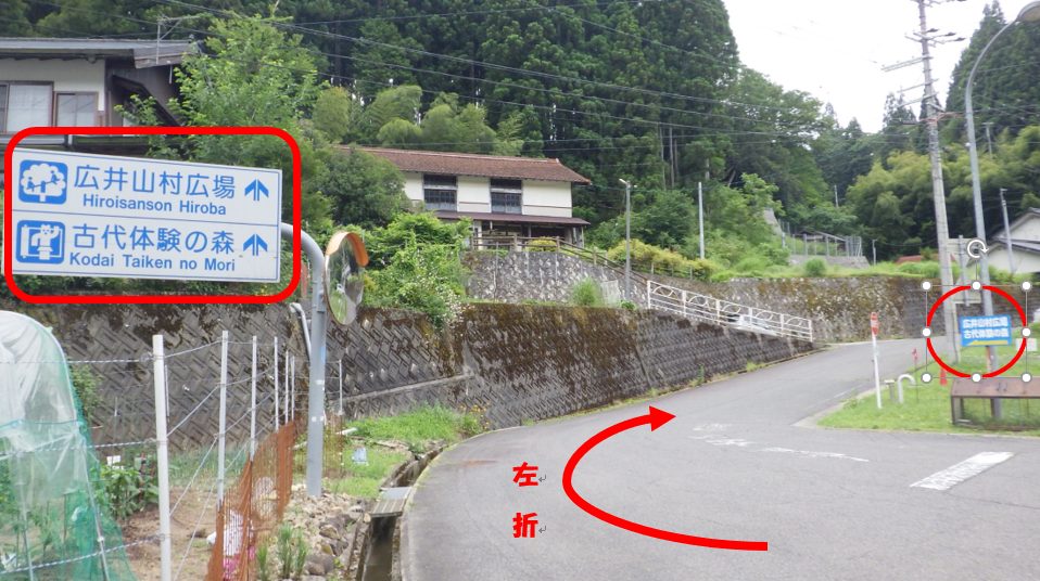 左折と書かれた赤い矢印と2つの道路看板が赤線で囲われた田舎道の写真