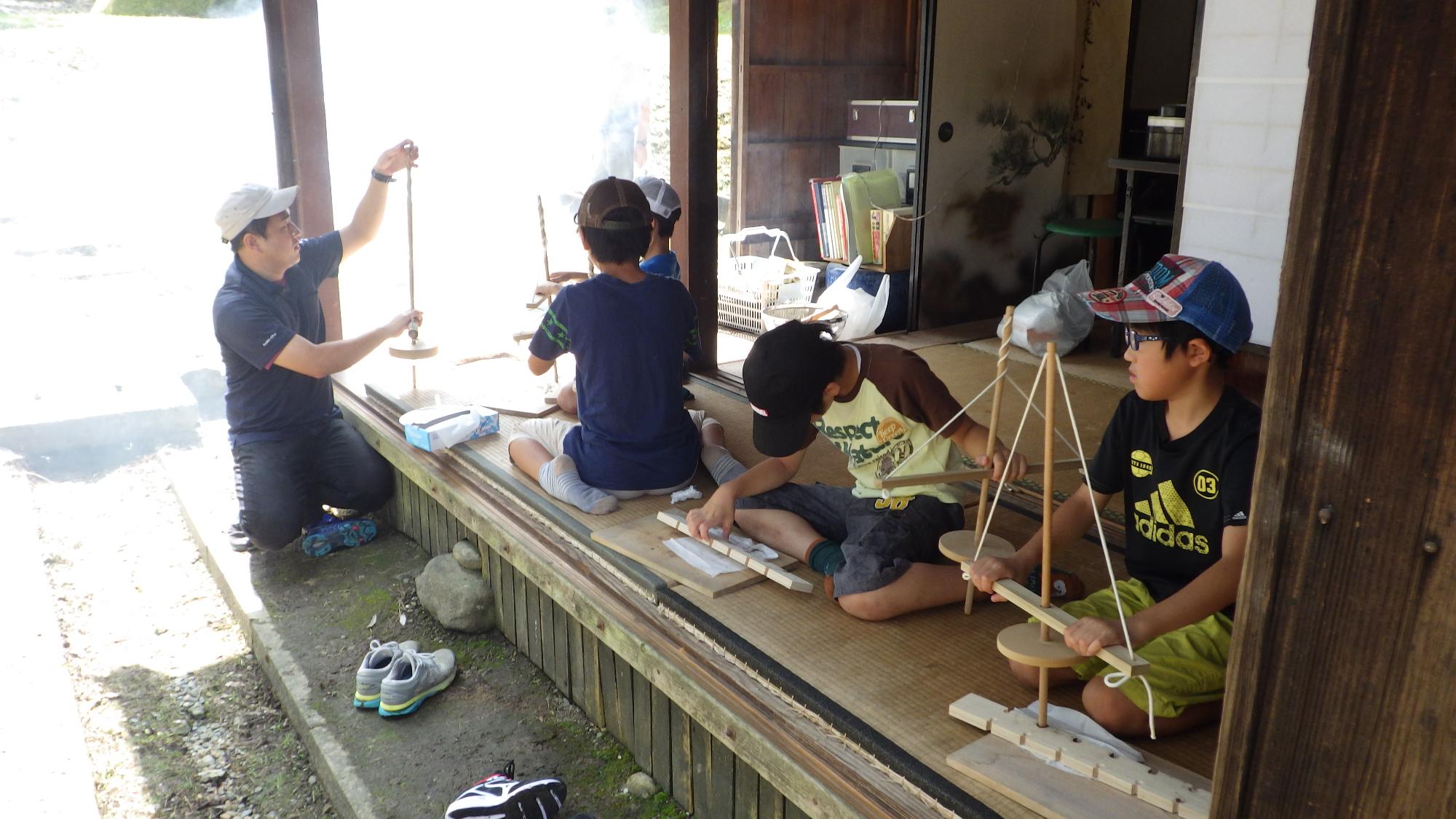 大人の人を見ながら木でできた道具を触る子供たちの写真