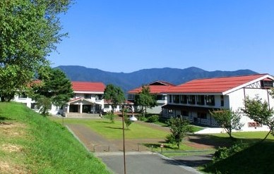 山に囲まれた広場に建てられた赤い屋根の建物の写真
