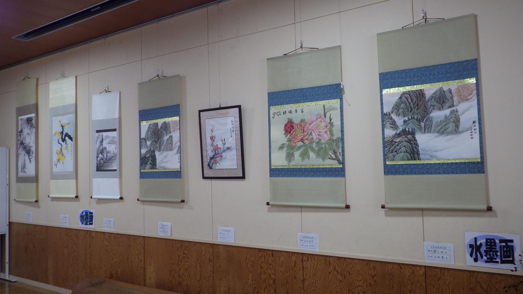 壁面に水墨画や日本画の掛け軸が並んで展示されている写真