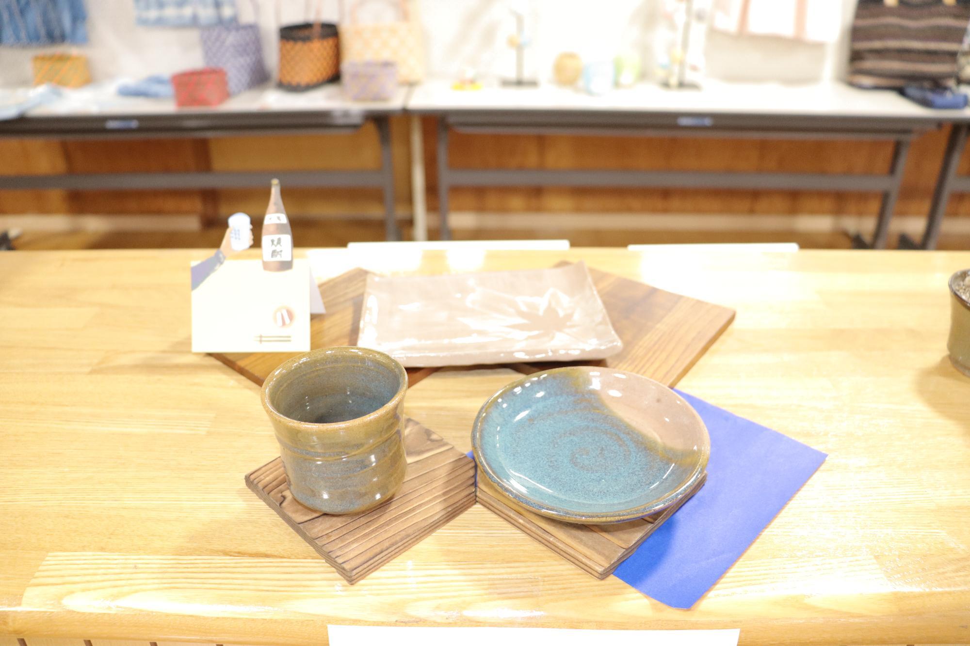 ハンガーに掛けられた藍染めや生成りの衣類と、机の上に並べられた毛糸や小物が展示されている写真