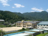 背景に緑豊かな大照山があり、小代小学校の校舎とプールが写っている写真