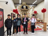 姫路駅構内に展示された神輿の前で写真を撮る先生と生徒たちの写真
