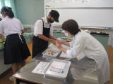 調理室の作業台でエプロン姿の生徒たちが調理の手順を確認しながら作業している写真