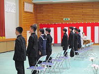 体育館で制服姿の生徒たちが少し緊張した様子で整列して起立している様子の写真