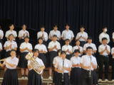 体育館の舞台上で制服姿の生徒たちが楽器を持って集合している様子の写真