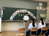 教室の黒板前で生徒が演台に立って発表している様子の写真