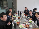 家庭科室で調理実習の料理を囲んで笑顔で食事をする生徒たちの写真
