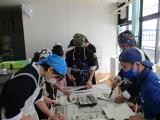 調理実習で生徒たちが講師と一緒に魚をまな板の上で下ごしらえしている写真
