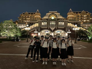 綺麗にライトアップされたディズニーランド入口のエントランスゲート前で、制服姿の学生たちがポーズを取りながら集合写真を取っている様子の写真