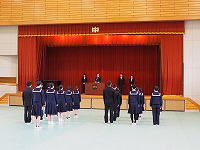 体育館で制服姿の生徒たちが壇上に向かって整列して入場している様子の写真