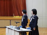 体育館の壇上で制服姿の生徒が司会進行をしている様子の写真