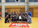体育館で黒いユニフォーム姿の部活動の生徒たちが集合して記念撮影している写真