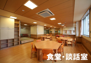 左下に白い文字で食堂・談話室と書かれているテーブルと椅子が並ぶ食堂兼談話室の室内を写した写真