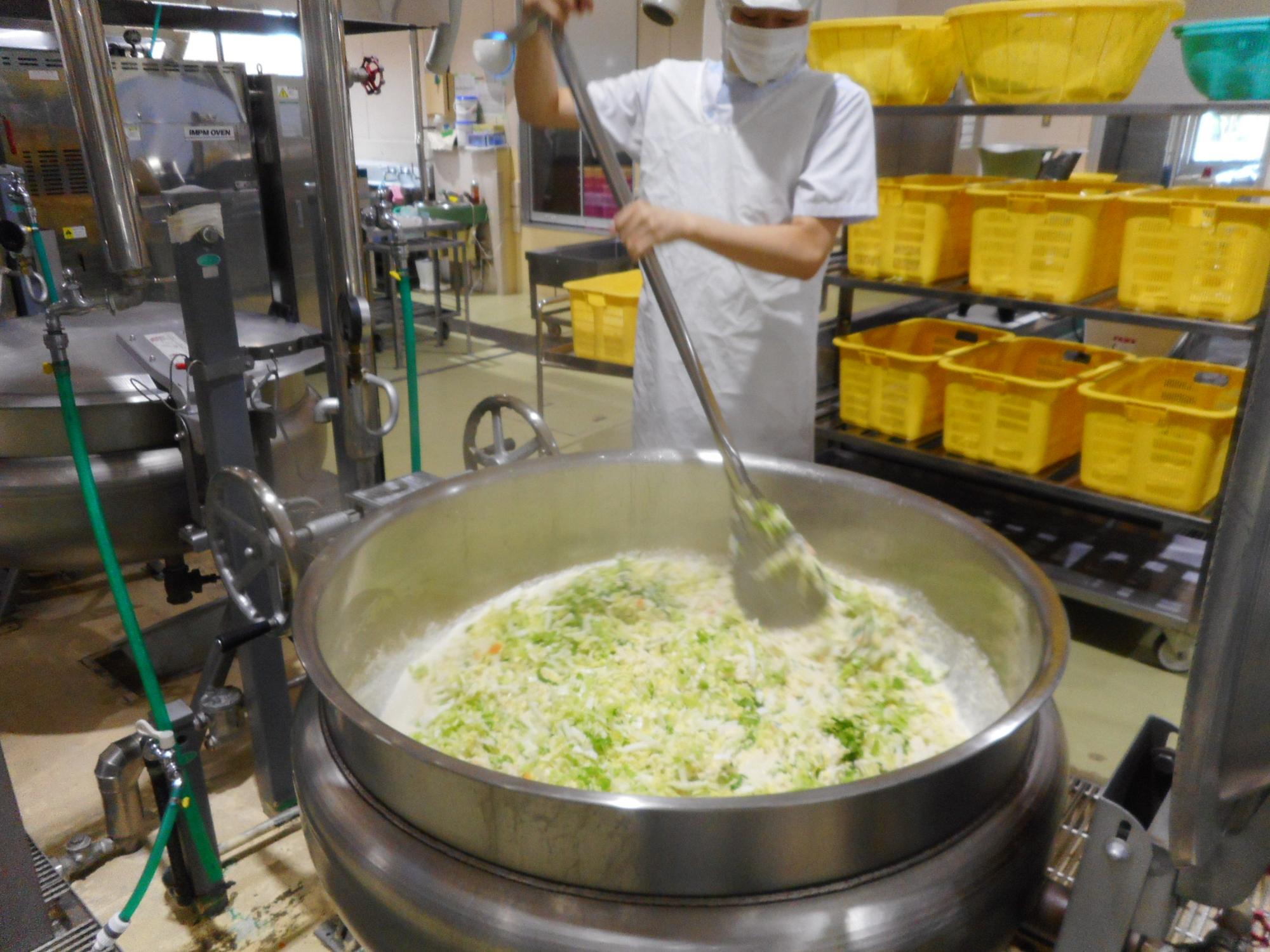 室内で調理員が器具を用いて食材を茹でている様子の写真