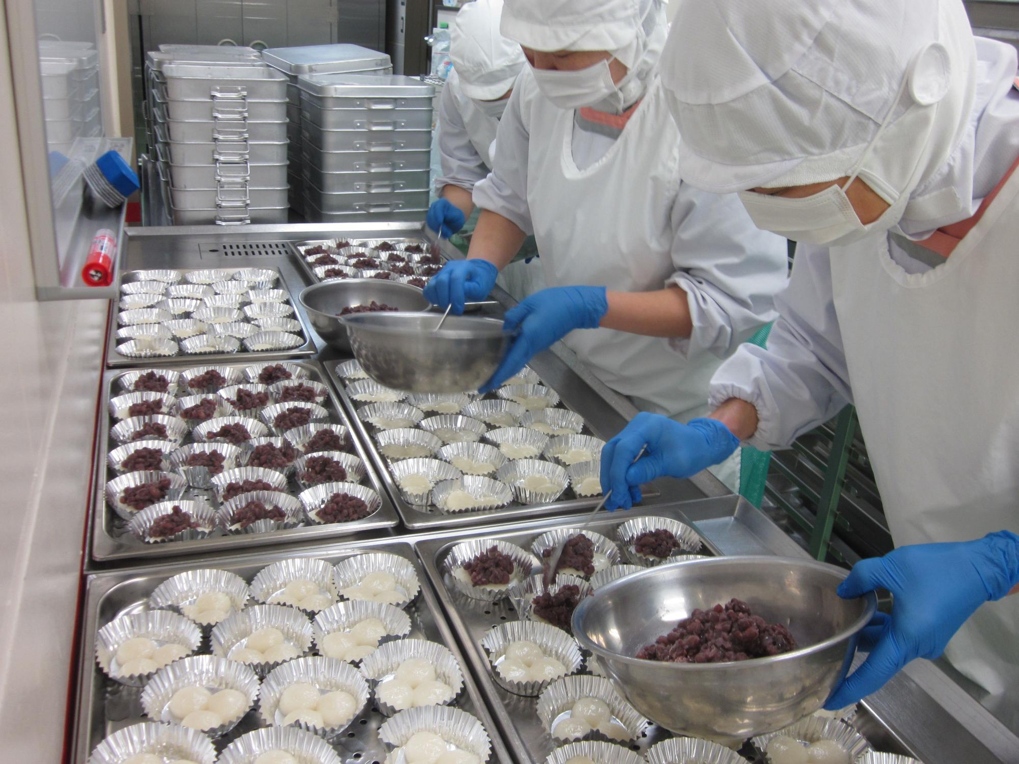 室内で調理員たちがスプーンを用いてあんこを配置している様子の写真