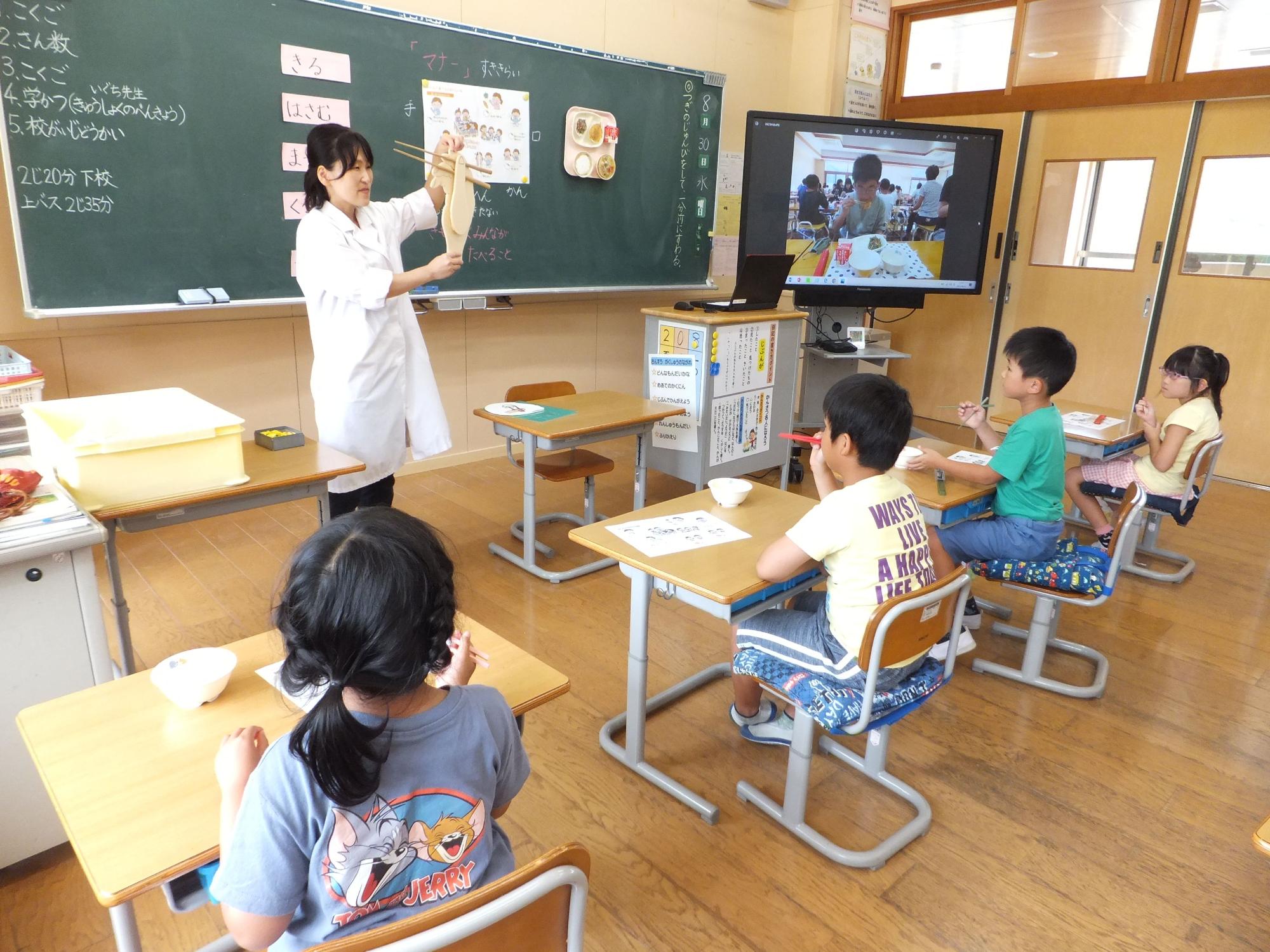 教室で教諭が児童たちに説明を行っている様子の写真