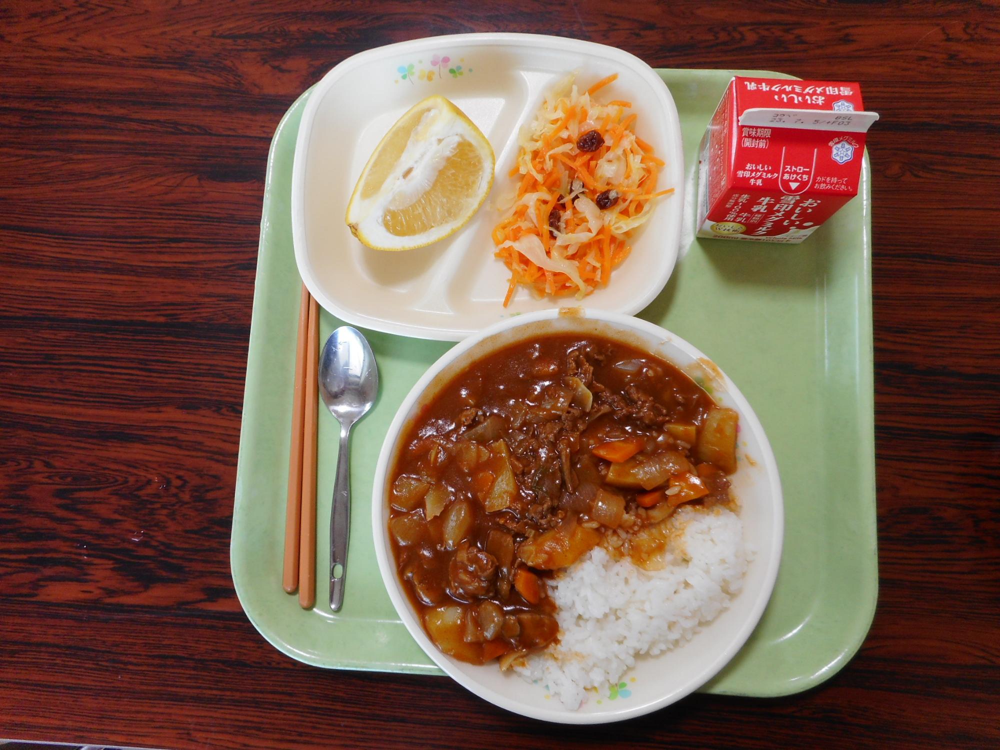 茶色の机の上にカレーとデザートと牛乳が置いてある写真