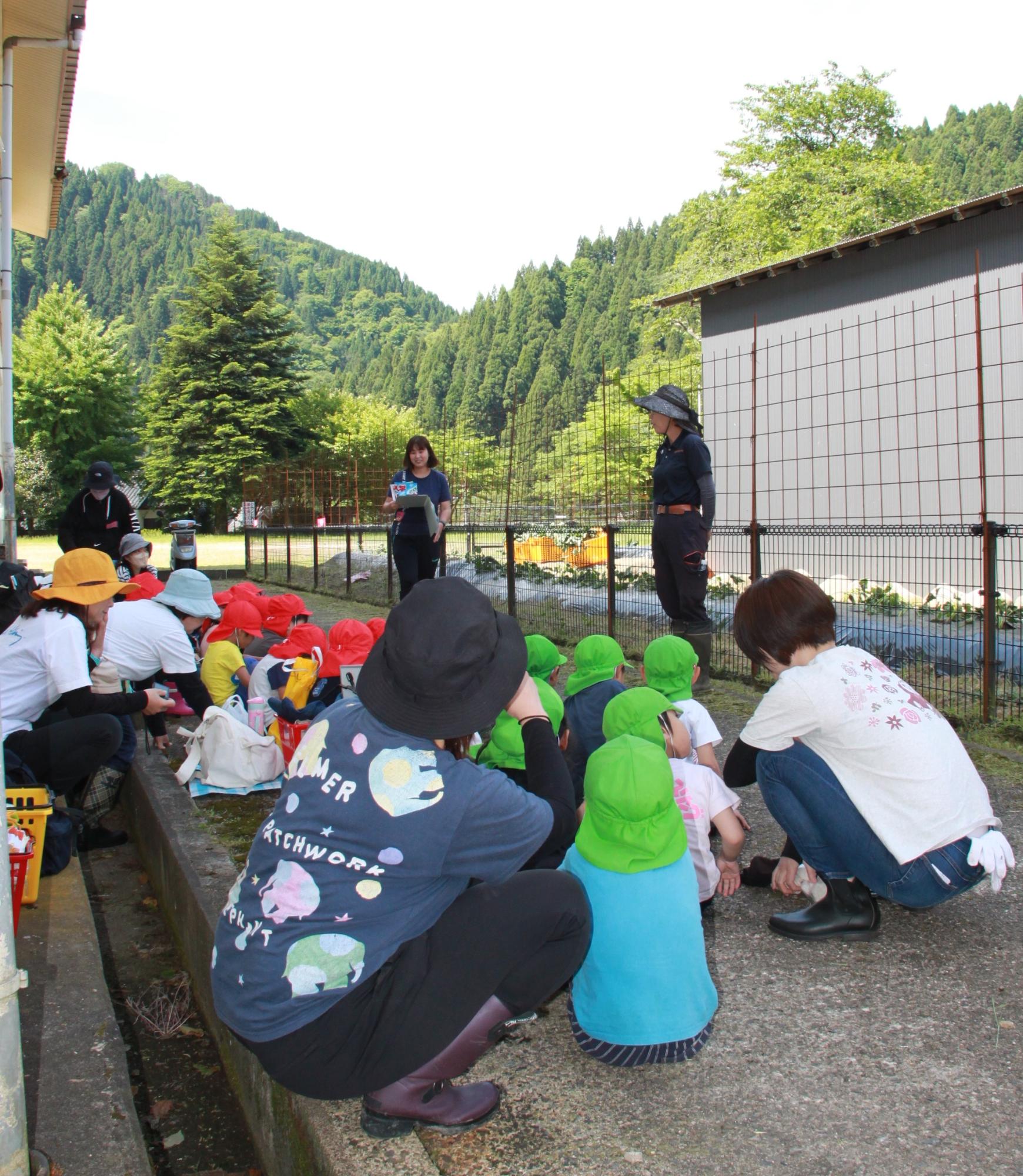 畑で園児たちが指導員の話を聞いている様子の写真