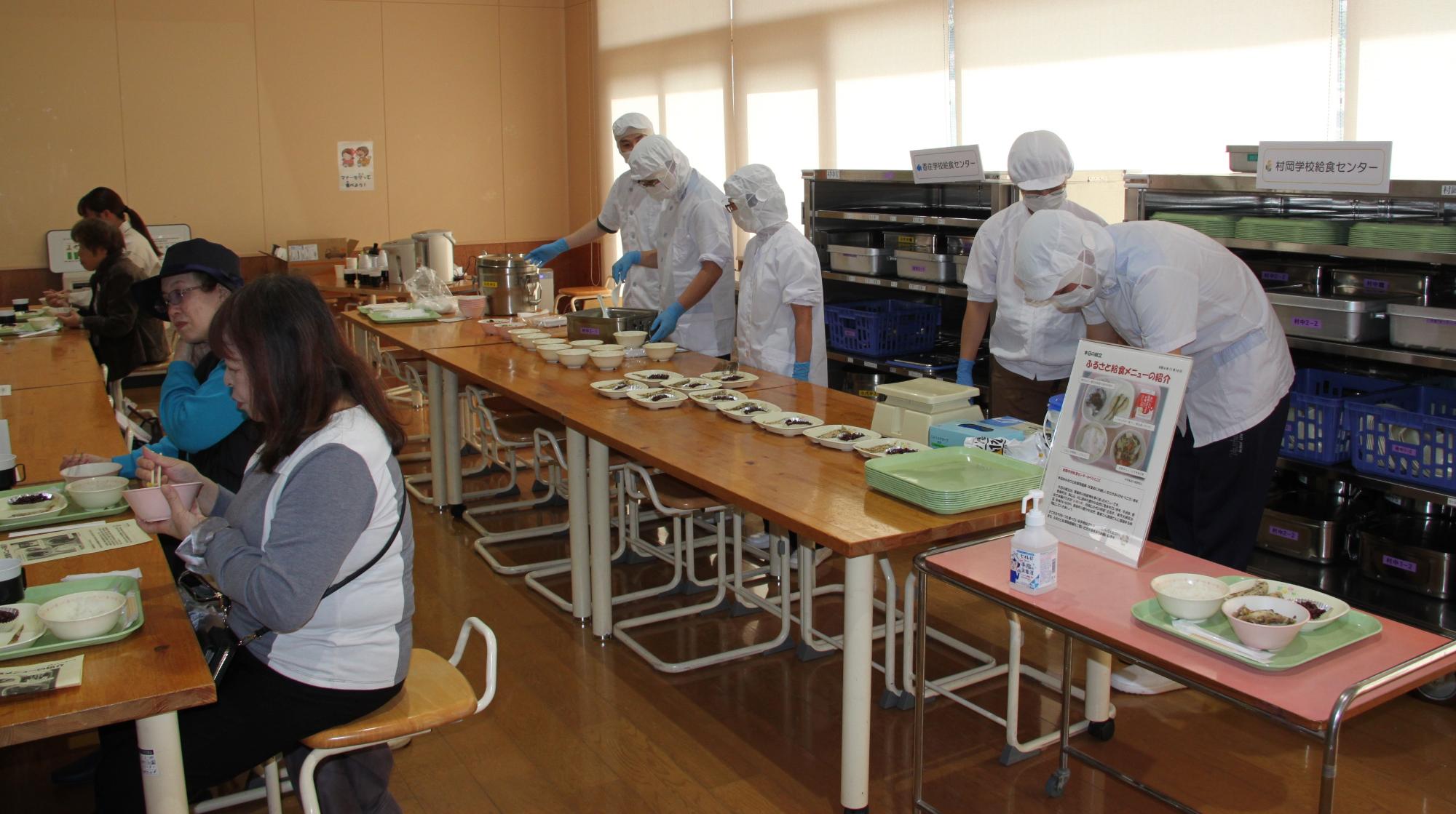 室内で割烹着を着た職員が配膳を行っている様子の写真