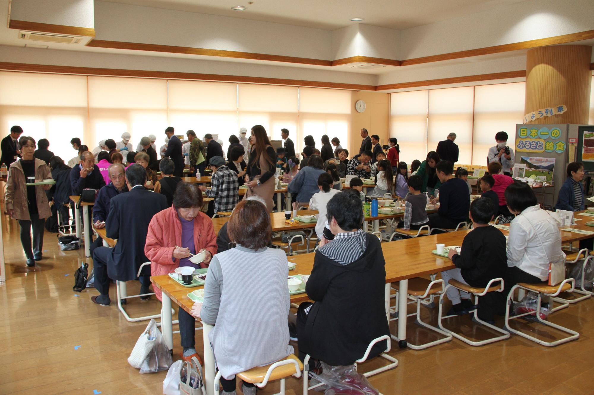 室内で遠くに列を作って並んでいる人たちと大人たちが食事を取っている様子の写真