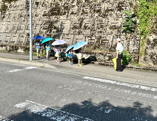 外で児童たちが傘をさしながら歩道で止まっている様子の写真