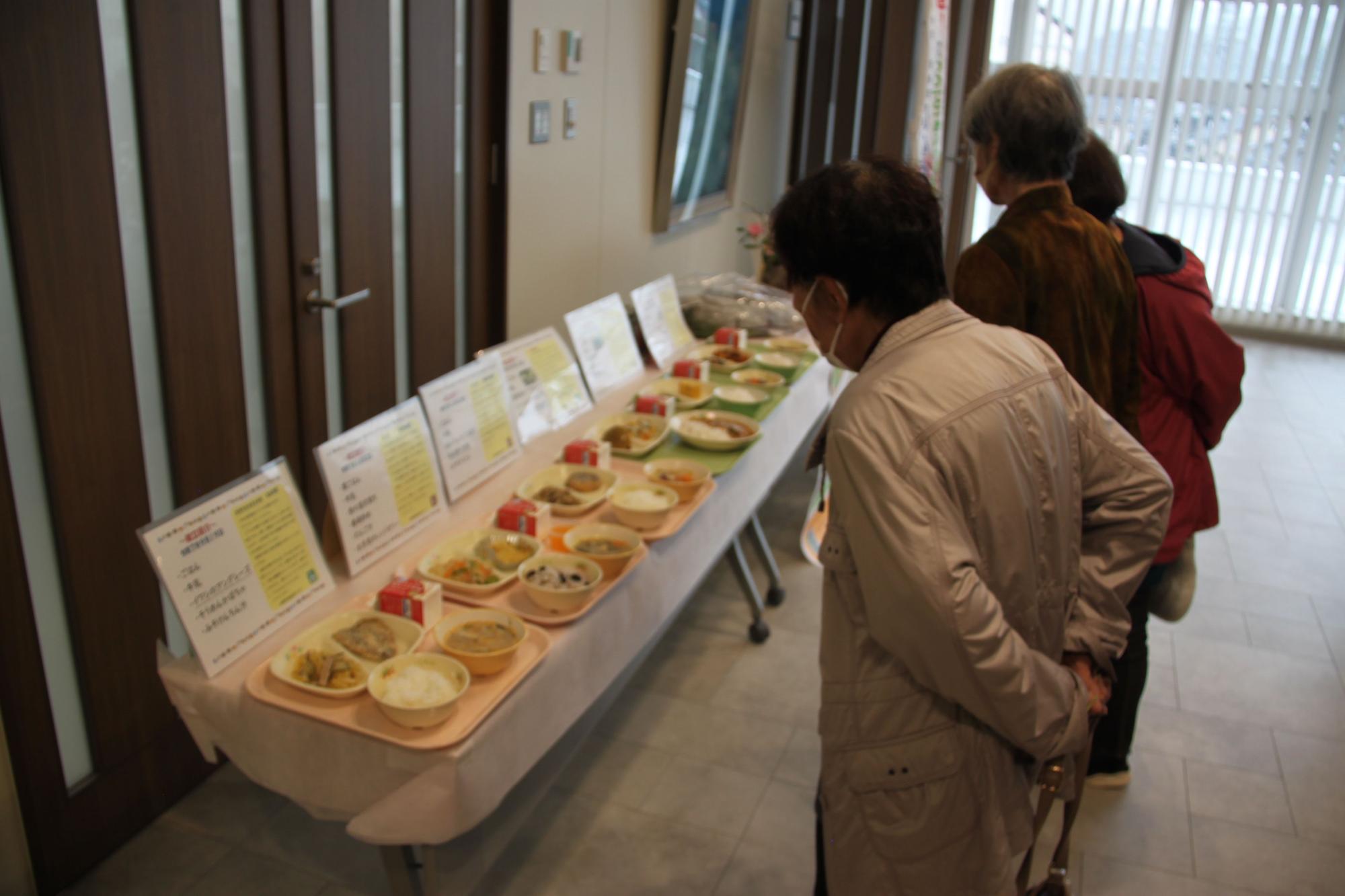 机に並べられた様々な給食を拝見している参加者の写真