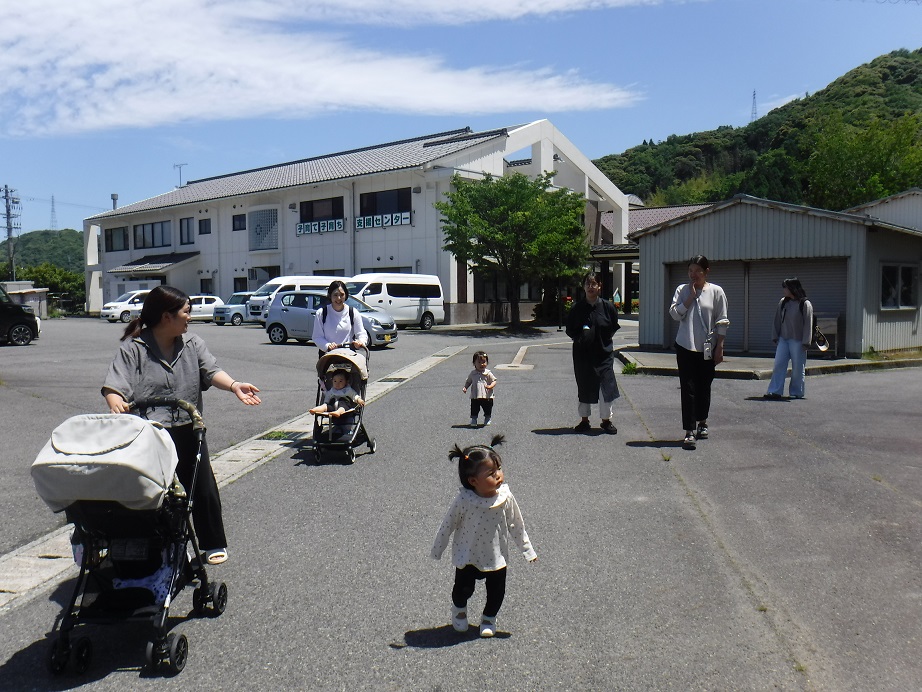 子育て子育ち支援センターと書かれた張り紙がある建物の手前で幼児と親が複数組歩いている様子の写真