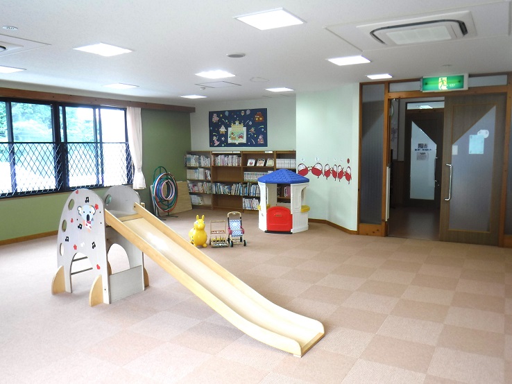 床がタイル状の布で、滑り台などの遊具や本棚がある香住子育て・子育ち支援センターの室内の写真