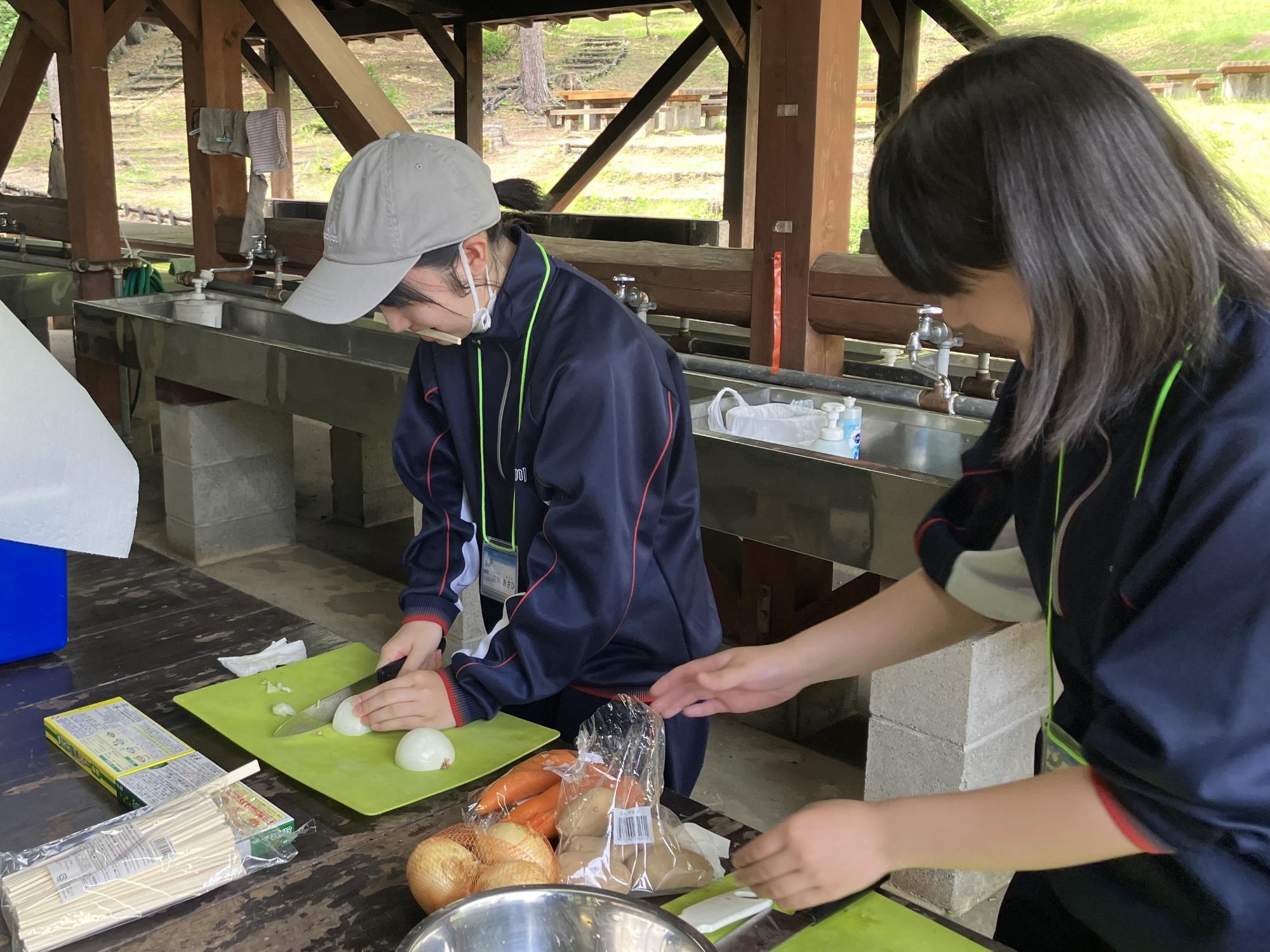 屋外の炊事場でカレーを作っている中学生の写真