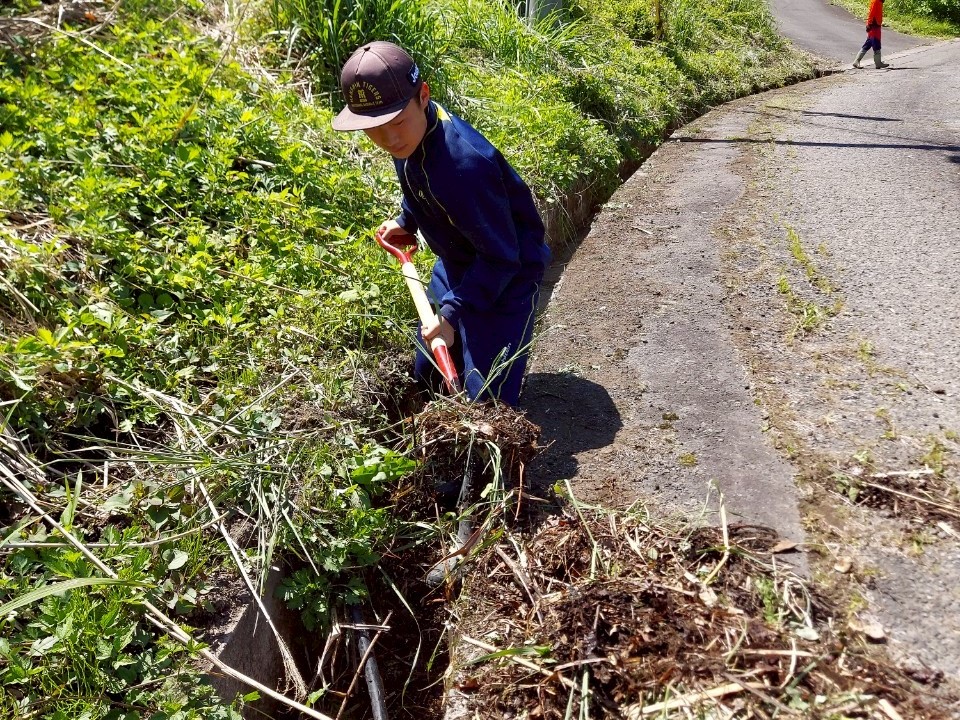 側溝の枯れ木や枝をスコップで外に出している中学生の写真