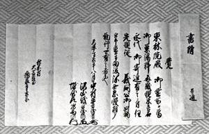 縦に折り目のついた紙に墨で文字が書かれている写真