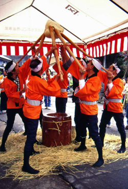 棒でうすから餅を高く掲げる6人のつき手たちの写真