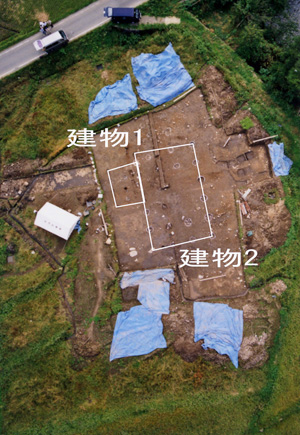 所々にビニールシートが置かれた土地に白い枠線や「建物1」「建物2」が書かれている航空写真