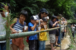 流しそうめんのそうめんをつかみこちらを見つめる子供の写真