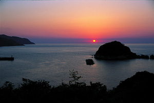 水平線近くに太陽のある海に浮かぶ島の写真