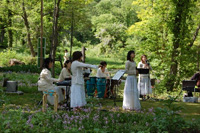 森林の広場で楽器の演奏やコーラスをしている人たちの写真