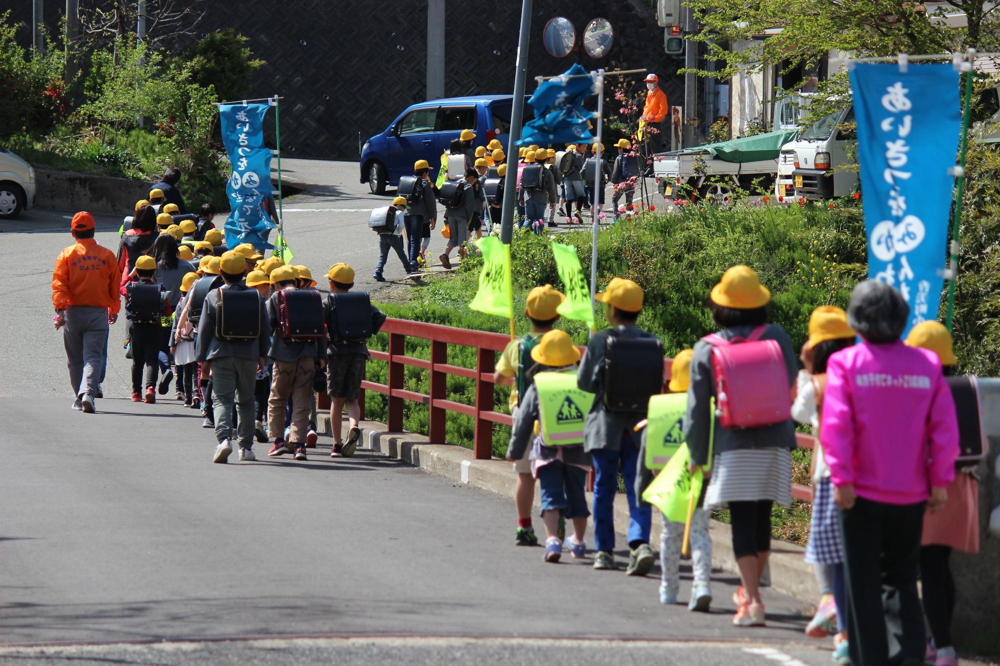 列になって道を歩く黄色い帽子を被った児童達の写真